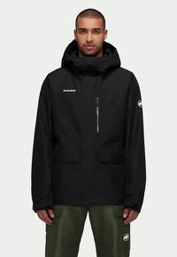 Άνδρας με μαύρο φούτερ με κουκούλα και τσέπη με φερμουάρ στο στήθος, και πράσινα παντελόνια, ενάντια σε απλή προσφορά.