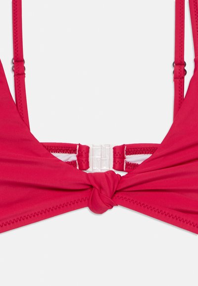 Top bikini rosso con spalline regolabili, dettaglio a nodo al centro e hardware in plastica trasparente. Texture liscia e cuciture minime.
