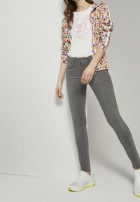 Šedé skinny džíny v kombinaci s bílým tričkem s růžovým logem a mikinou na zip s květinovým vzorem. Oblečeno s bílými teniskami.