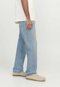 Jeans de mezclilla de lavado claro con un corte relajado, piernas rectas y un desvanecimiento sutil. Llevados con zapatos estilo mocasín en color beige.
