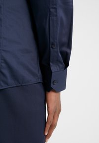 Navyblauw langemouw shirt met een gladde textuur, knoopmanchetten en een getailleerde pasvorm, voorzien van een zijnaaddetail en contrasterende knopen.