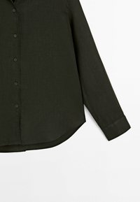 Blouse vert foncé à manches longues, avec un devant boutonné, un col et un ourlet arrondi. Fabriquée en tissu texturé avec des boutons noirs.