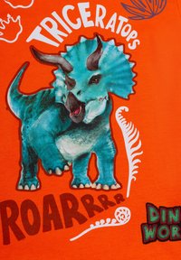 Maglietta arancione brillante con una grafica di un triceratopo teal con texture e dettagli accurati, accanto al testo "ROARRRRR" e "DINOWORLD".