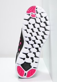 Suela de zapatilla atlética negra con un patrón texturizado en blanco, acentuada con grips hexagonales en rosa. Superficie lisa y diseño flexible.
