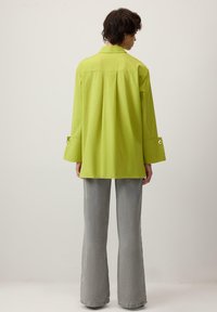 Laimerohelise värvi lühike särk krae ja külgmiste lõhikute ning heledate hallide lõhenevate teksadega, nähtav tagantpoolt.