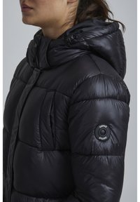 Černá péřová bunda s lesklým povrchem, s kapucí, zipem zepředu, bočními kapsami a kulatou nášivkou na levém rukávu.