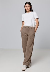 Pantalon marron à jambes larges en tissu texturé, associé à un haut blanc à manches courtes. Comprend des poches latérales et une fermeture à bouton à l'avant.