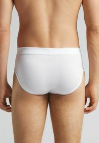 Witte katoenen slips met een zachte tailleband, minimale bedekking en een gladde textuur, die een aansluitende silhouet benadrukt.