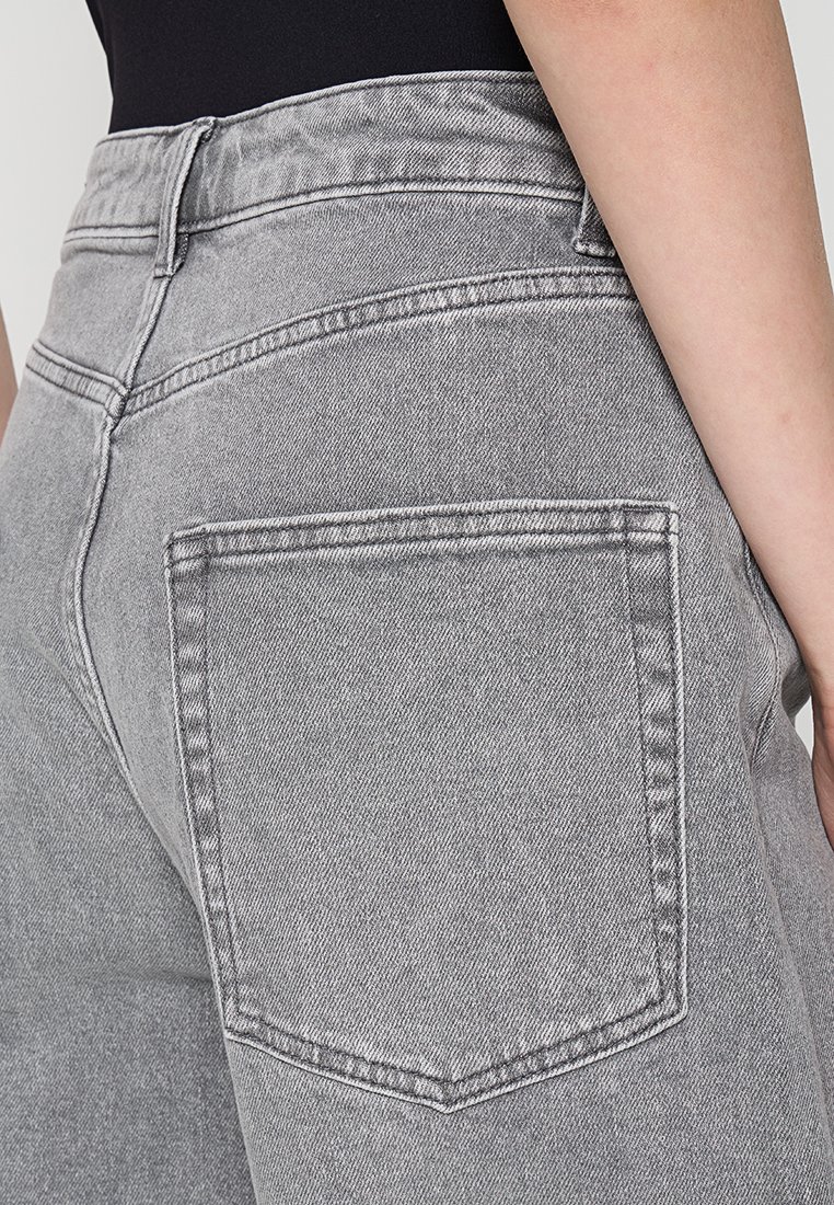 Jeans in denim grigio con vita alta, dettagli sulle tasche posteriori e cuciture a contrasto. Il tessuto ha una finitura testurizzata.