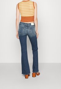 Uplatněný ribbed pletený top v oranžové a žluté barvě s krátkým designem, v kombinaci s modrými vysoce pasovými rozšířenými džíny a oranžovými podpatky s vzorem.