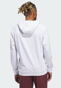 Valkoinen huppari, jossa teksturoitu kangas, rento malli hupulla, pitkät hihat ja resorit hihoissa. Päällä viininpunaiset housut, kuva otettu takaa.