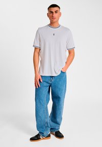 White t-shirt with black striped ribbed collar and cuffs, worn with blue baggy jeans and black sneakers with gum soles.