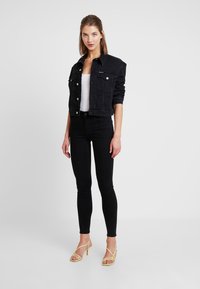 Svart denimjakke med en kort design, frontlommer og sølvknapper, kombinert med svarte skinny jeans og gule stroppehæler.