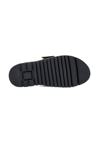 Black rubber shoe sole with textured surface, featuring horizontal and vertical ridges for grip, and a raised logo detail in the center.