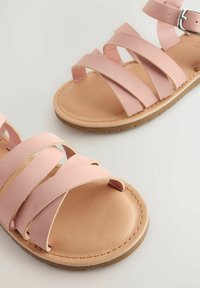 Sandali sintetici rosa con cinturini, suola piatta e sottopiede beige testurizzato. Presentano una fibbia laterale per una vestibilità regolabile.