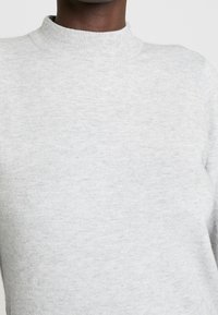 Maglione grigio chiaro con un collo alto, realizzato in morbido tessuto a maglia. Caratterizzato da una leggera trama e un design semplice senza motivi o decorazioni.
