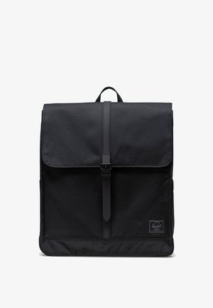 Mochila negra con solapa plegable, hecha de un tejido duradero, que cuenta con un cierre de hebilla y un parche de logo cosido en la parte frontal.
