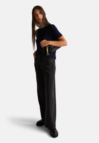 Námořnický top s krátkým rukávem, široké černé džíny, černé robustní boty a černá taška s klíčenkou v žlutém akcentu. Jednoduchá, moderní silueta.