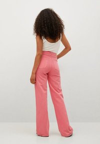 Pantalon large rose à taille haute, en tissu de coton. Comprend des poches arrière et une texture lisse, associé à un débardeur blanc.