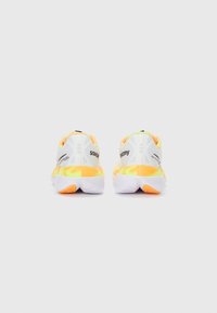 Zapatos deportivos blancos con acentos amarillos y naranjas, con una parte superior texturizada y un logotipo prominente en el talón. Diseño de suela ligera.