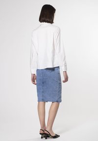 Camicia bianca a maniche lunghe con colletto abbinata a una gonna in denim blu chiaro lunghezza ginocchio, con tasche posteriori e vestibilità dritta. Sandali neri con tacco.