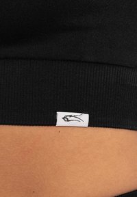 Zwarte ribbelstof band met een wit label waarop een zwarte lijntekening staat. Close-up weergave die de textuur en stiksels benadrukt.