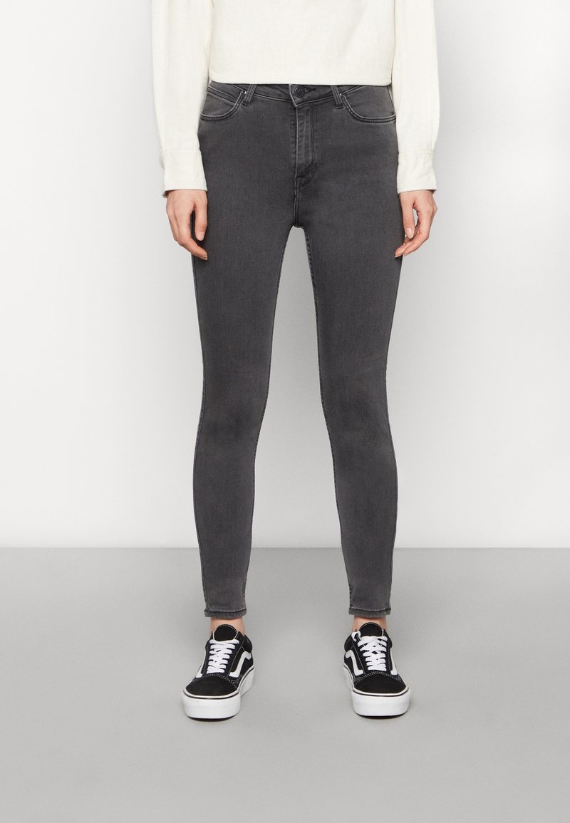 Jeans skinny grises con cinco bolsillos, pasadores para cinturón y una cinturilla a media altura. Combinados con zapatillas negras y blancas y un suéter crema.
