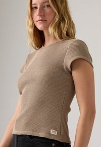 Camiseta de punto acanalado beige con mangas cortas. Presenta un cuello redondo y una pequeña etiqueta de marca roja en el dobladillo. Tejido texturizado de mezcla de algodón.