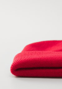 Berretto in maglia rosso con un motivo texturizzato e un risvolto. Il materiale sembra morbido e caldo, con un colore uniforme e vivace.