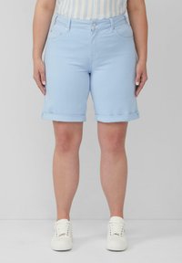 Shorts en denim bleu clair avec des ourlets retroussés, cinq poches et une fermeture par bouton. Texture lisse et design ajusté. Des sneakers blanches sont portées.