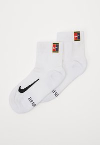 Fehér sportzokni, fekete Nike logóval és színes, téglalap alakú címkével, rajta a Nike logóval.