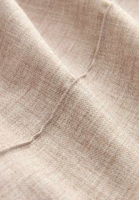 Vaalean beige kangas, jossa on hienovarainen kuvio, pehmeä pinta ja hento kiilto, esittäen päällekkäisiä taitoksia ja saumoja.
