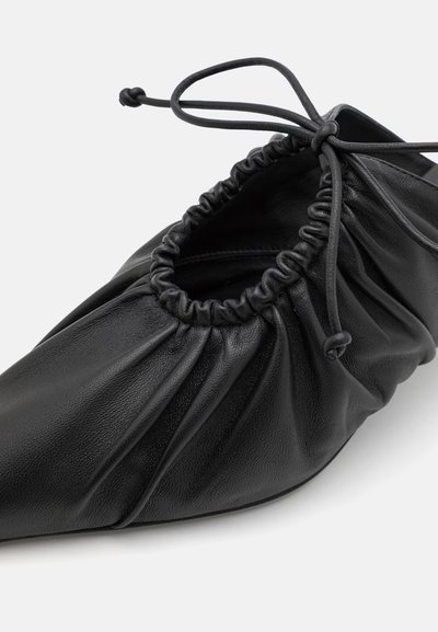 Black leather shoe with a gathered design and elastic top, pointed toe, and narrow sole. Features adjustable ties for fit.