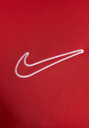 Rode stof met een gladde textuur, voorzien van een witte, geborduurde Nike swoosh-logo aan de linkerkant. Het ontwerp is minimalistisch en sportief.