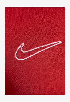 Roter Stoff mit glatter Textur, der auf der linken Seite ein weißes, gesticktes Nike-Swoosh-Logo zeigt. Das Design ist minimalistischer und sportlich.