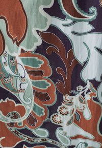 Tissu à motifs présentant de grands motifs floraux en marron, vert menthe et bleu canard, sur un fond violet foncé. Apparence texturée.