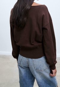 Pull marron oversize avec un ourlet côtelé et un col large, associé à un jean en denim bleu clair avec une coupe décontract ée.