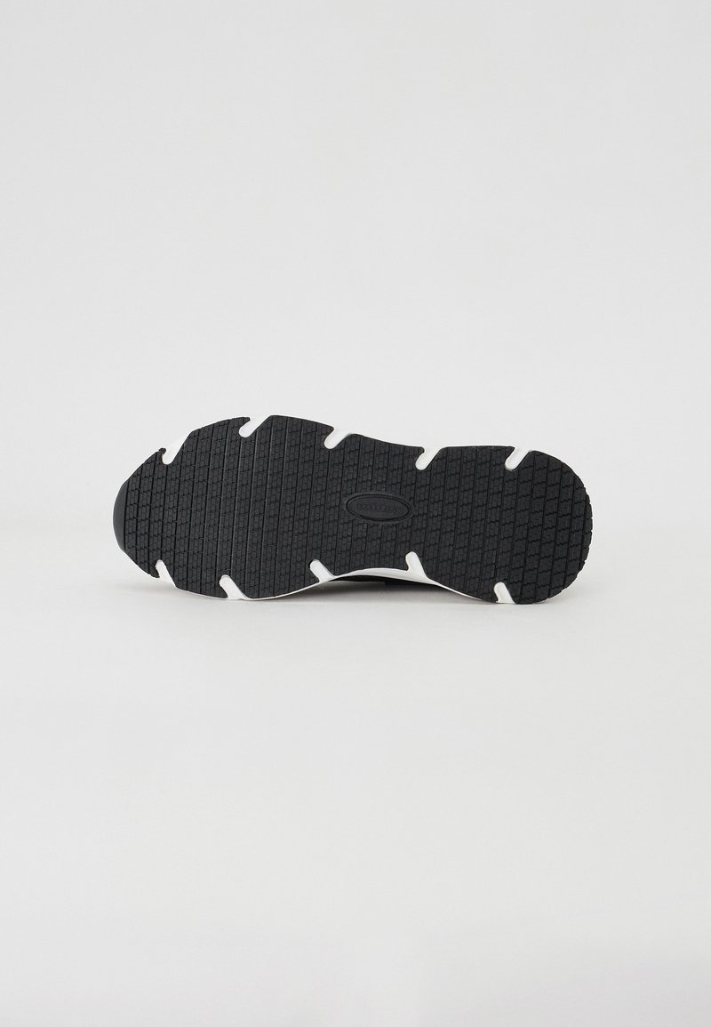 Schwarze Gummisohle mit strukturiertem Griff und weißen Akzenten vor einem schlichten, hellen Hintergrund.