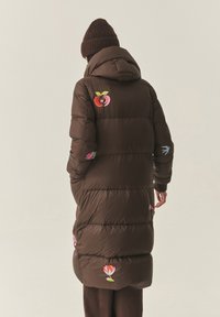 Barna pufi kabát kapucnival, színes gyümölcs- és virághímzéssel díszítve. Sima tapintású, térdig érő, oldalzsebes kialakítás.