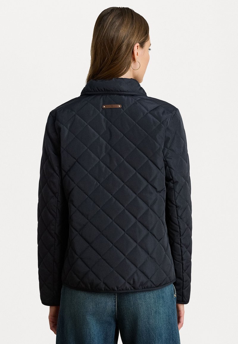 Veste matelassée noire avec un col structuré, dotée de pièces métalliques au dos. Texture lisse et manches à coupe droite.