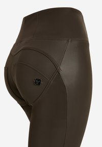 Leggings in finta pelle marrone con vita alta, con dettagli di cuciture curve e una piccola etichetta nera vicino alla tasca.