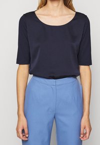 Haut bleu marine à manches courtes avec un col rond, fabriqué en tissu lisse. Assorti à un pantalon bleu clair, bien ajusté, avec des poches latérales.