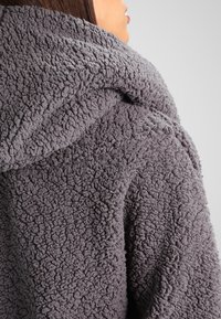 Felpa con cappuccio grigio, in pile texturizzato, con un grande cappuccio e una superficie morbida e a anelli. Presenta una vestibilità comoda e nessuna minuteria o accentuazione visibile.