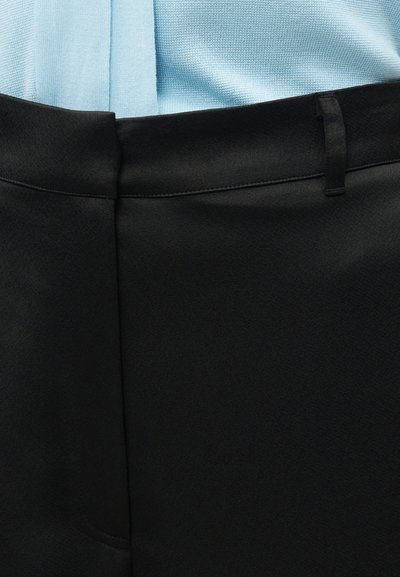 Εγγύς λήψη μέσης μαύρου παντελονιού με θηλιά ζώνης, συνδυασμένο με ανοιχτό μπλε υφασμάτινο τοπ με υφή, που είναι φορεμένο μέσα.