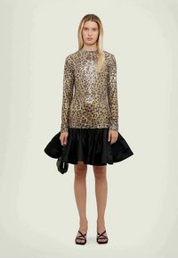 Vestido dourado brilhante com lantejoulas, mangas longas e uma saia preta de cetim godê. Apresenta um decote redondo e um corpete justo.