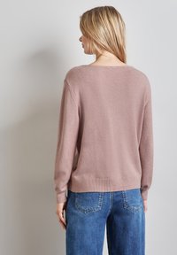 Pullover rosa chiaro in maglia con una vestibilità comoda, orlo e polsini a coste, e scollatura a punto. Abbinato a jeans in denim blu.