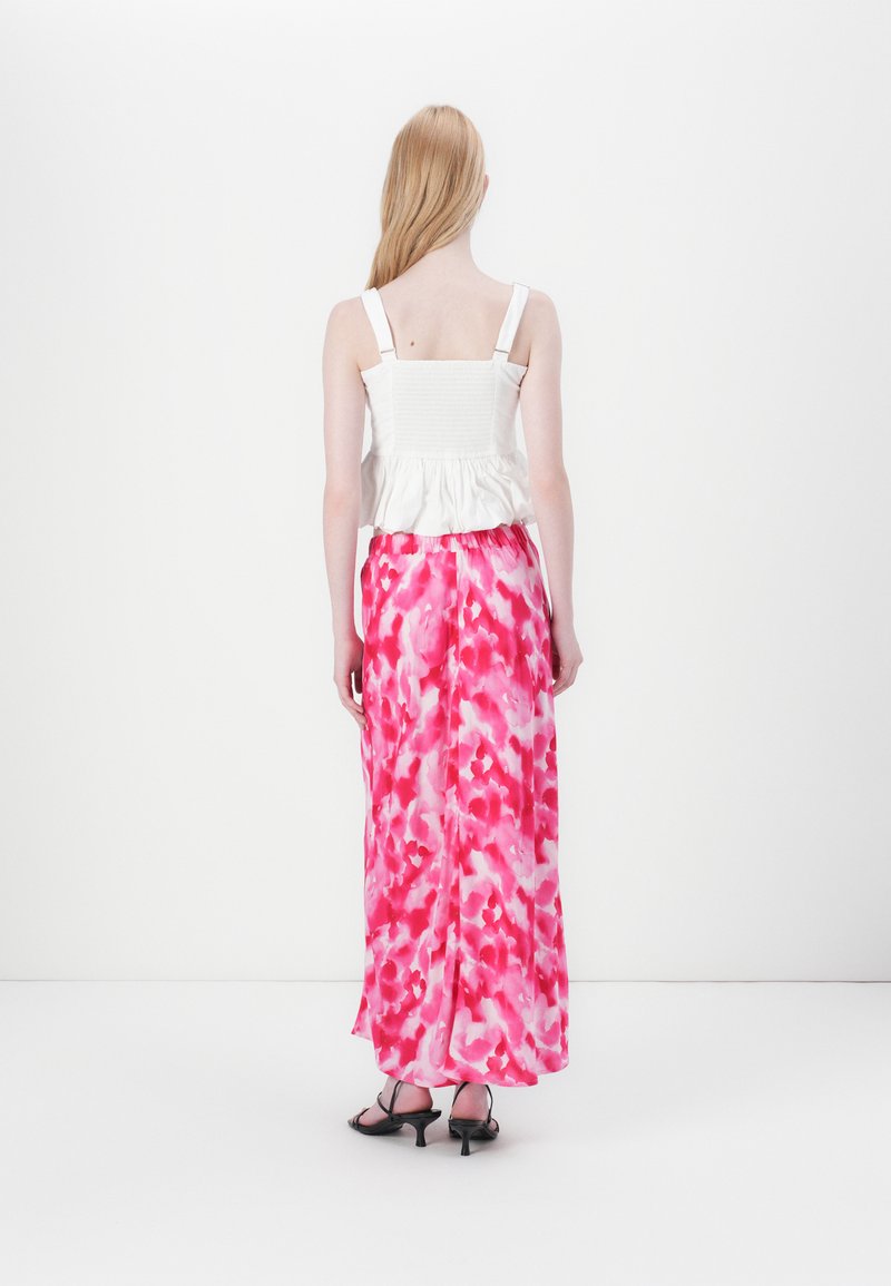 Haut peplum blanc avec des bretelles fines, associé à une longue jupe rose tie-dye présentant une silhouette fluide et une texture subtile.