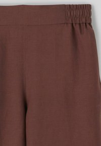 Pantalon en lin marron à taille élastique, avec une texture lisse, une coupe large et un minimum de couture sur la taille et les coutures latérales.