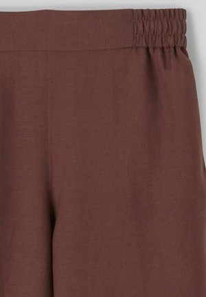 Pantalon en lin marron à taille élastique, avec une texture lisse, une coupe large et un minimum de couture sur la taille et les coutures latérales.