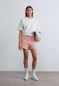 Sweat-shirt oversize en coton blanc, short rose, baskets blanches, chaussettes à la cheville, avec une pochette beige. Comprend un branding minimaliste et des tatouages.
